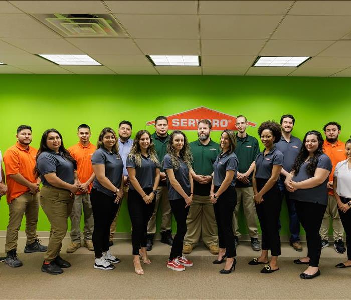 Group of SERVPRO employees wearing SERVPRO polo shirts smiling, standing against a green wall with the SERVPRO logo.